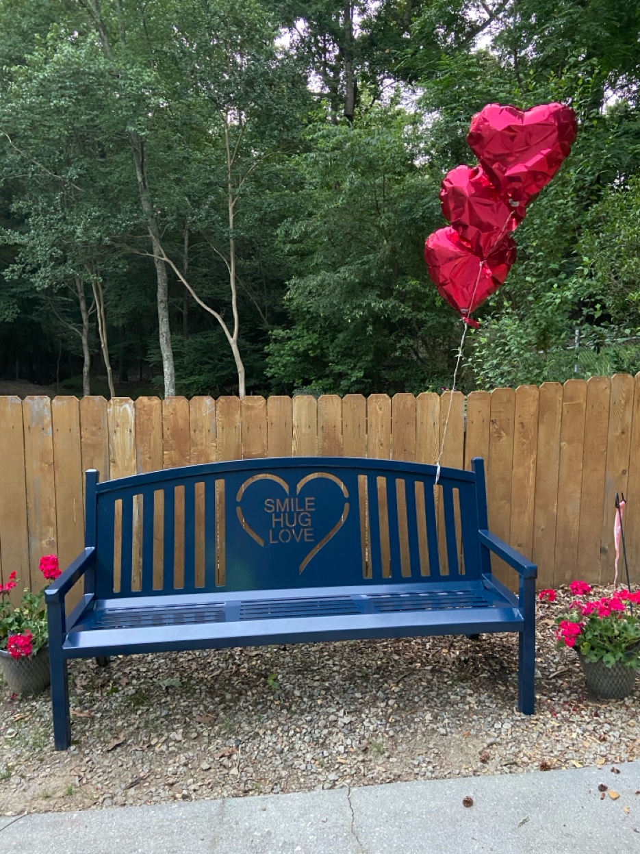 The Love Like Amy bench at the Lee family home in Dacula, Georgia — three red heart balloons floating above it, red geraniums on each side