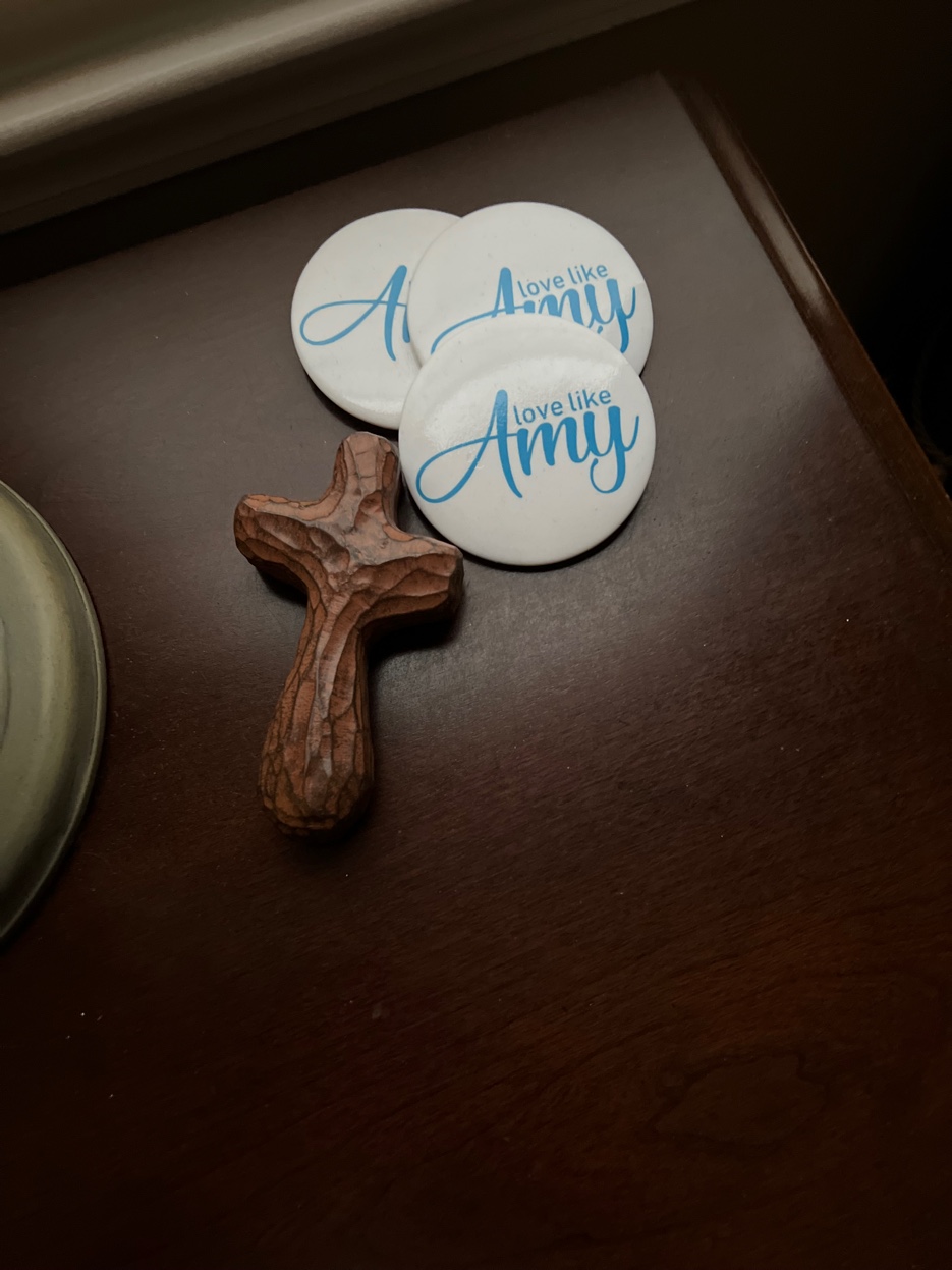 The Love Like Amy button — white with blue script — alongside a small wooden cross